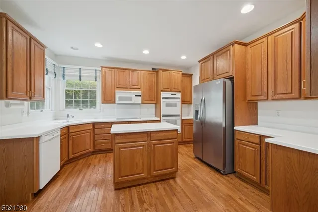 a kitchen with stainless steel appliances granite countertop a refrigerator a sink dishwasher a stove and white countertops with wooden floor