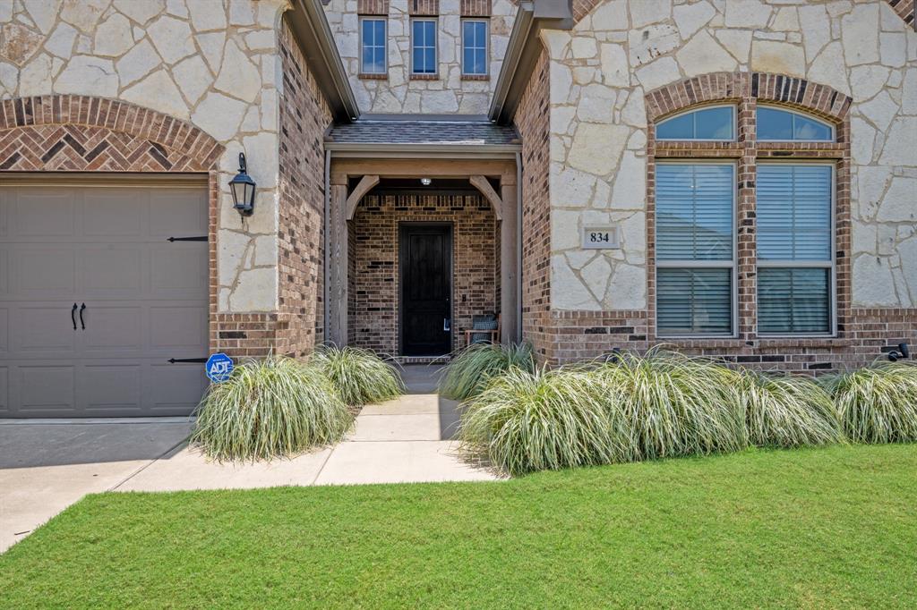 834 Rustic Trail Midlothian, TX 76065 - Photo 5 of 29 Beautiful stone-and-brick elevation creates an impressive first impression with timeless curb appeal. The covered front porch provides a warm and inviting entrance, while lush ornamental grasses and a manicured lawn enhance the professionally landscaped front yard.