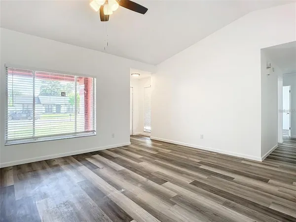 an empty room with wooden floor ceiling fan and windows