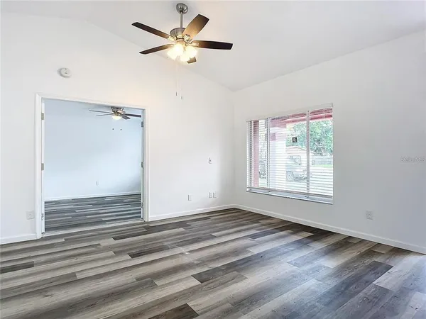 a view of an empty room with wooden floor and a ceiling fan