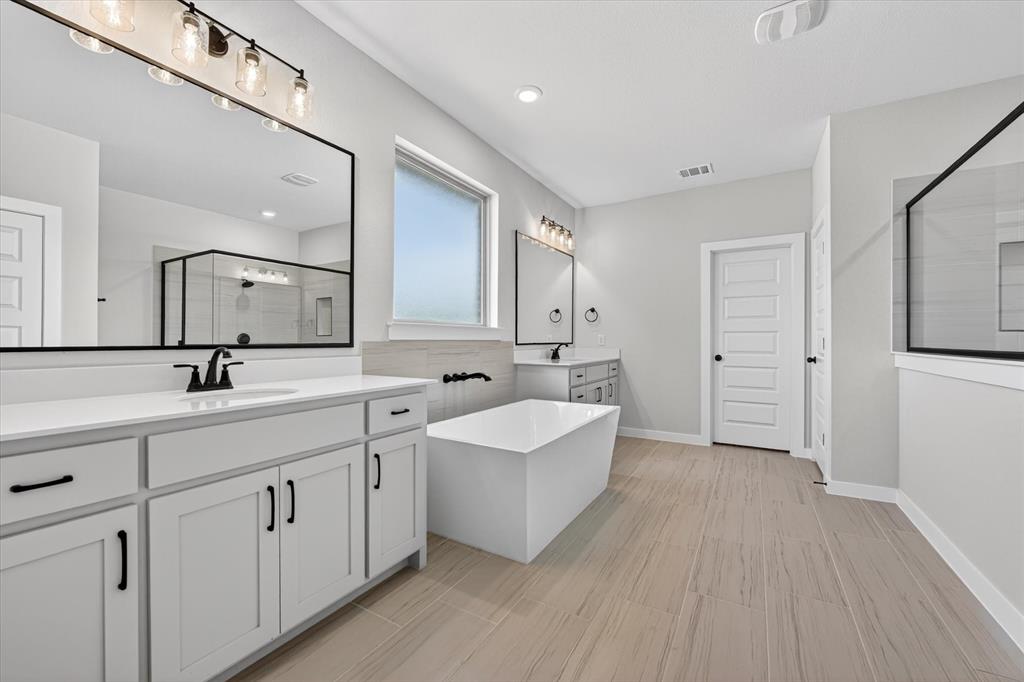 409 Mcalpine Springtown, TX 76082 - Photo 23 of 38 Bathroom featuring dual vanities, a freestanding soaking tub, a separate glass-enclosed shower, wood-finish flooring, and a frosted window
