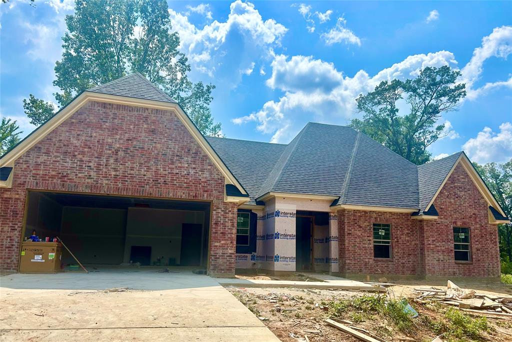 View of front of property with brick siding, driveway, and roof with shingles