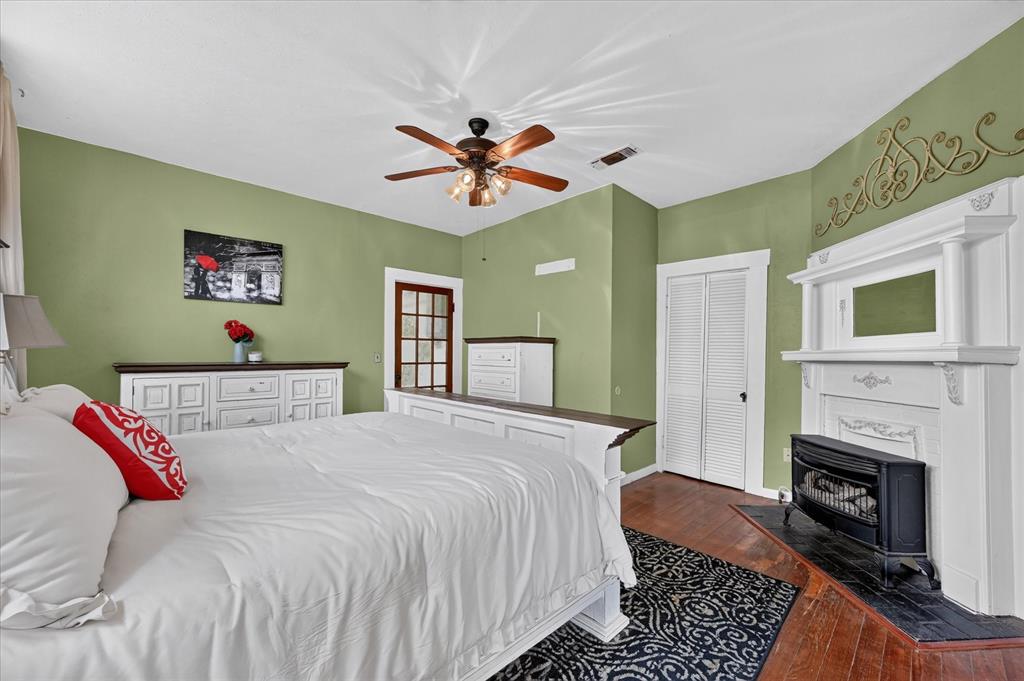 304 East Main Street Itasca, TX 76055 - Photo 18 of 38 Hardwood flooring, white architectural fireplace with dark hearth, ceiling fan, louvered closet doors, and a glass-paneled door