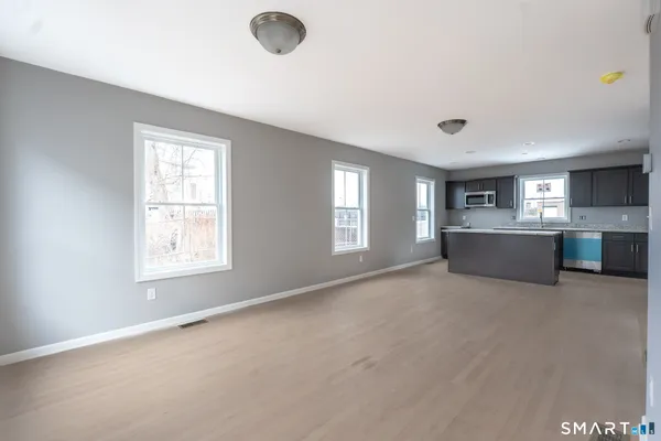 a view of an empty room with a window and kitchen view