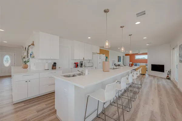a large white kitchen with a large counter top space a sink stainless steel appliances and cabinets