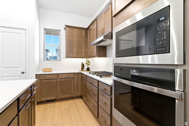 7243 West Terraine Road West Jordan, UT 84081 - Photo 6 of 31 Kitchen featuring a built-in stainless steel microwave and oven, a white subway tile backsplash, light wood-finish flooring, and warm-toned cabinetry