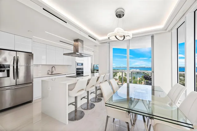 a kitchen with stainless steel appliances granite countertop a refrigerator a stove top oven a dining table and chairs with wooden floor