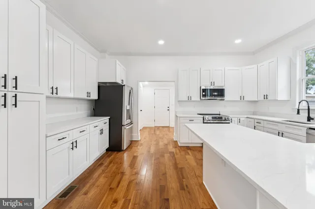 a kitchen with stainless steel appliances granite countertop a refrigerator a stove top oven a sink dishwasher and white cabinets with wooden floor