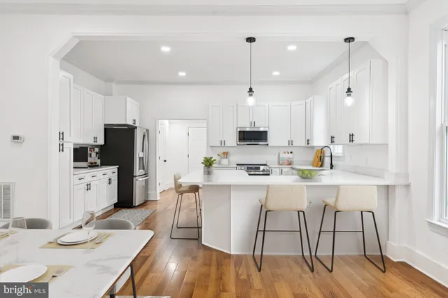 a kitchen with stainless steel appliances kitchen island granite countertop a sink a stove a refrigerator and white cabinets with wooden floor