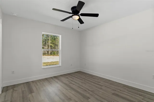 an empty room with wooden floor ceiling fan and windows