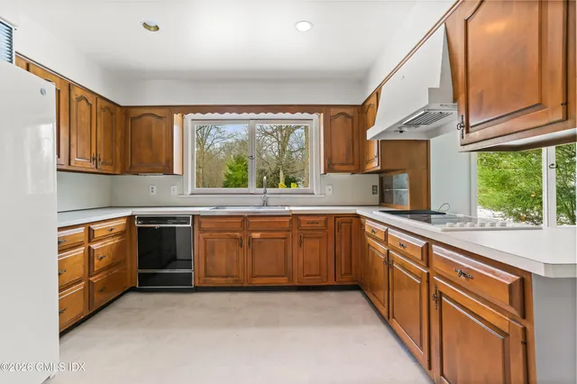 a kitchen with stainless steel appliances granite countertop wooden cabinets a stove a sink and a large window