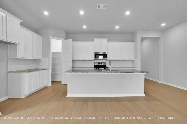 a view of kitchen with stainless steel appliances granite countertop a stove a sink a refrigerator and white cabinets with wooden floor