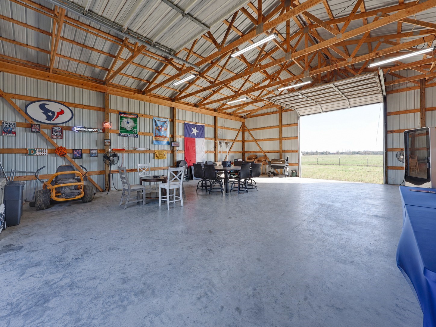 1055 County Road Weimar, TX 78962 - Photo 21 of 33 Spacious barn interior with open concrete floors, high ceilings, and roll-up door access. Well-suited for entertaining, workshop space, storage, or flexible use, offering a comfortable setup for gatherings and country hobbies alike. This barn includes a tack room, overhead storage and plenty of electrical outlets.
