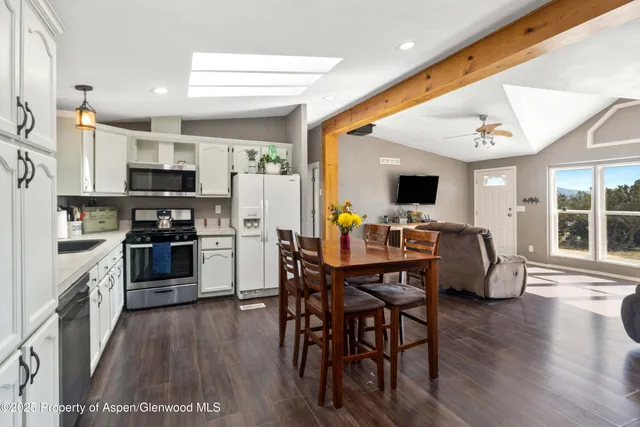 a kitchen with stainless steel appliances kitchen island granite countertop a stove top oven a sink a dining table and chairs with wooden floor