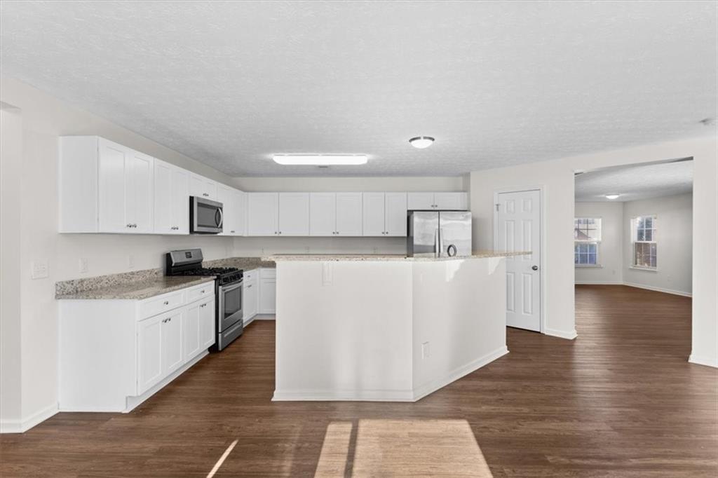 2068 White Top Road Southeast Lawrenceville, GA 30045 - Photo 14 of 41 a large white kitchen with kitchen island a stove a sink a refrigerator and white cabinets with wooden floor