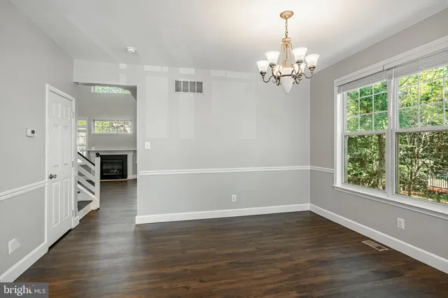 an empty room with wooden floor chandelier and windows