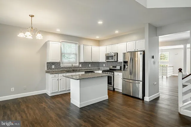 a kitchen with stainless steel appliances granite countertop a refrigerator a sink dishwasher a stove and white cabinets with wooden floor