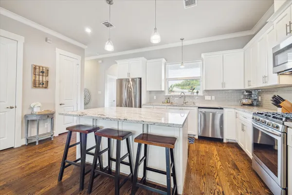 a kitchen with stainless steel appliances granite countertop a stove top oven a sink a dining table and chairs with wooden floor