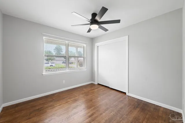 an empty room with wooden floor ceiling fan and windows