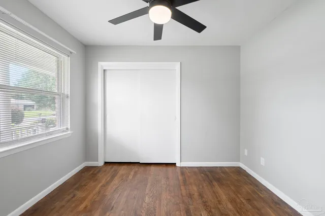 an empty room with wooden floor chandelier fan and windows
