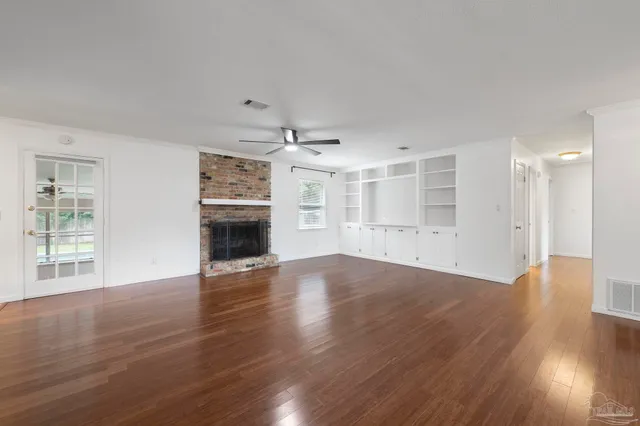 an empty room with wooden floor fireplace and windows