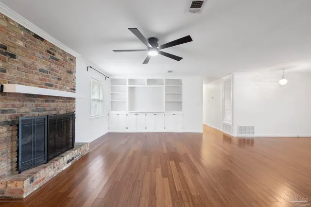 an empty room with wooden floor a ceiling fan and fireplace