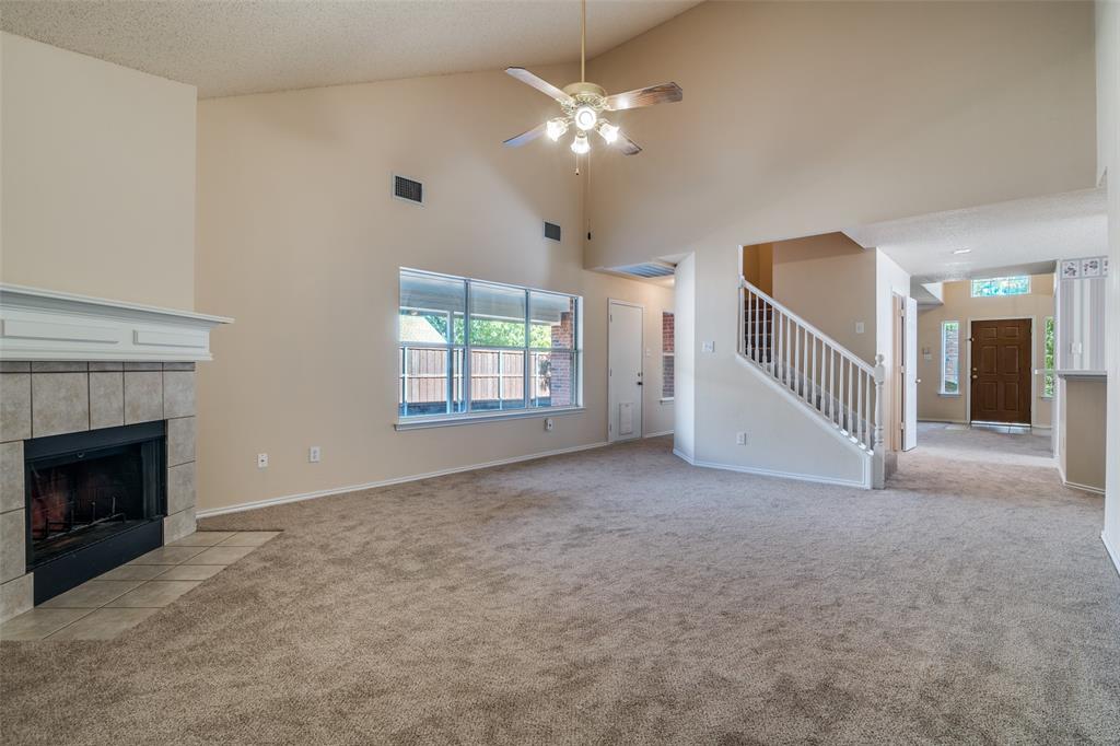 1202 Morrow Lane Allen, TX 75002 - Photo 9 of 35 Unfurnished living room with light colored carpet, stairway, vaulted ceiling, a ceiling fan, and a tile fireplace