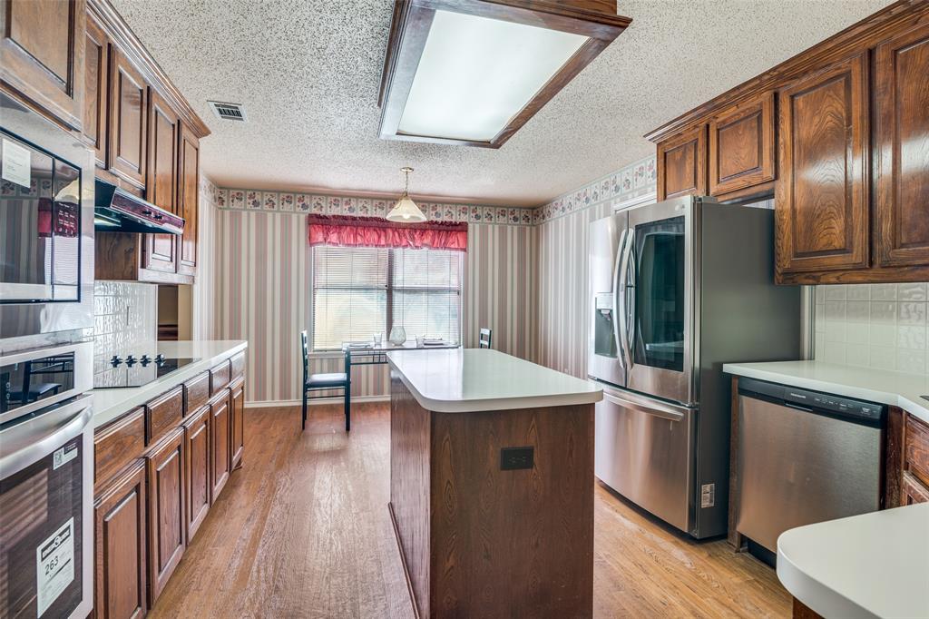 1202 Morrow Lane Allen, TX 75002 - Photo 10 of 35 Kitchen with tasteful backsplash, a center island, stainless steel appliances, wallpapered walls, and light countertops