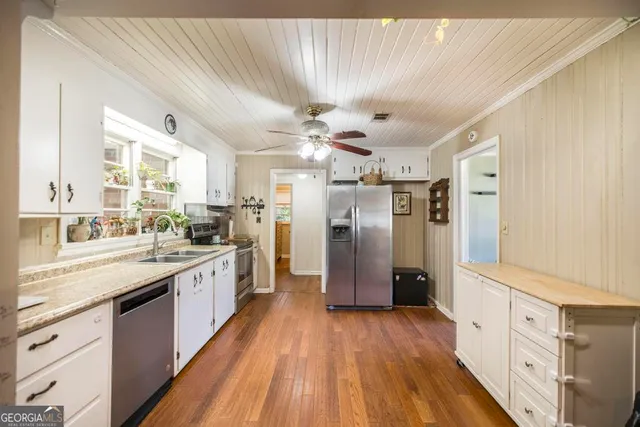 a large kitchen with stainless steel appliances a refrigerator a sink dishwasher a stove and white cabinets with wooden floor