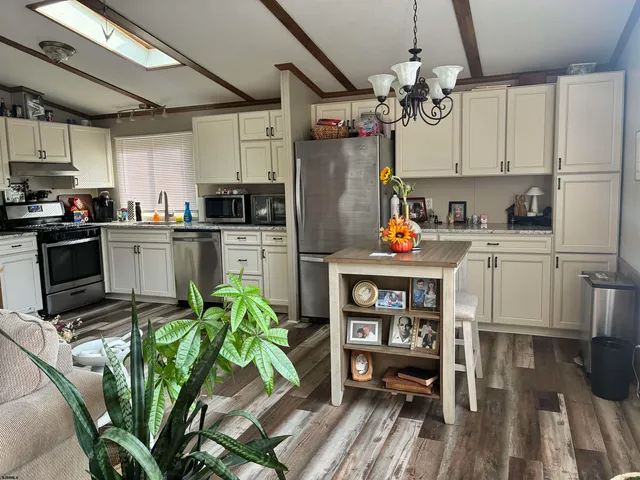 a kitchen with stainless steel appliances granite countertop a refrigerator a stove top oven a sink dishwasher and white cabinets with wooden floor