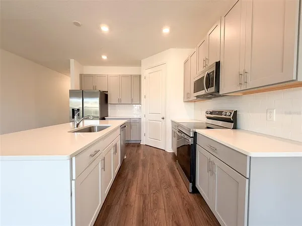 a kitchen with stainless steel appliances granite countertop a sink a stove top oven a refrigerator with white cabinets and wooden floor