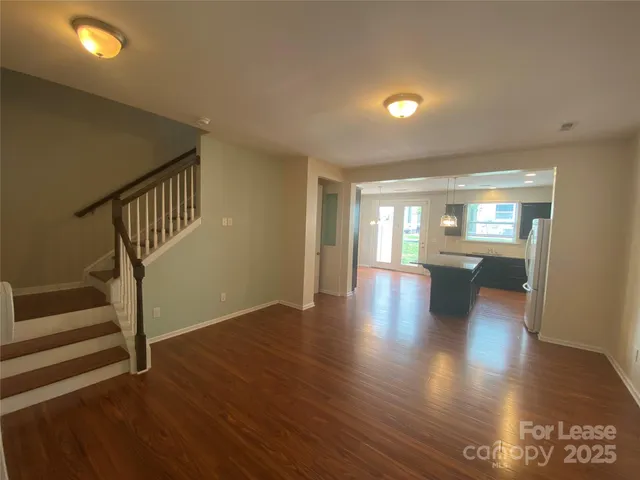 a view of an empty room with wooden floor and a kitchen