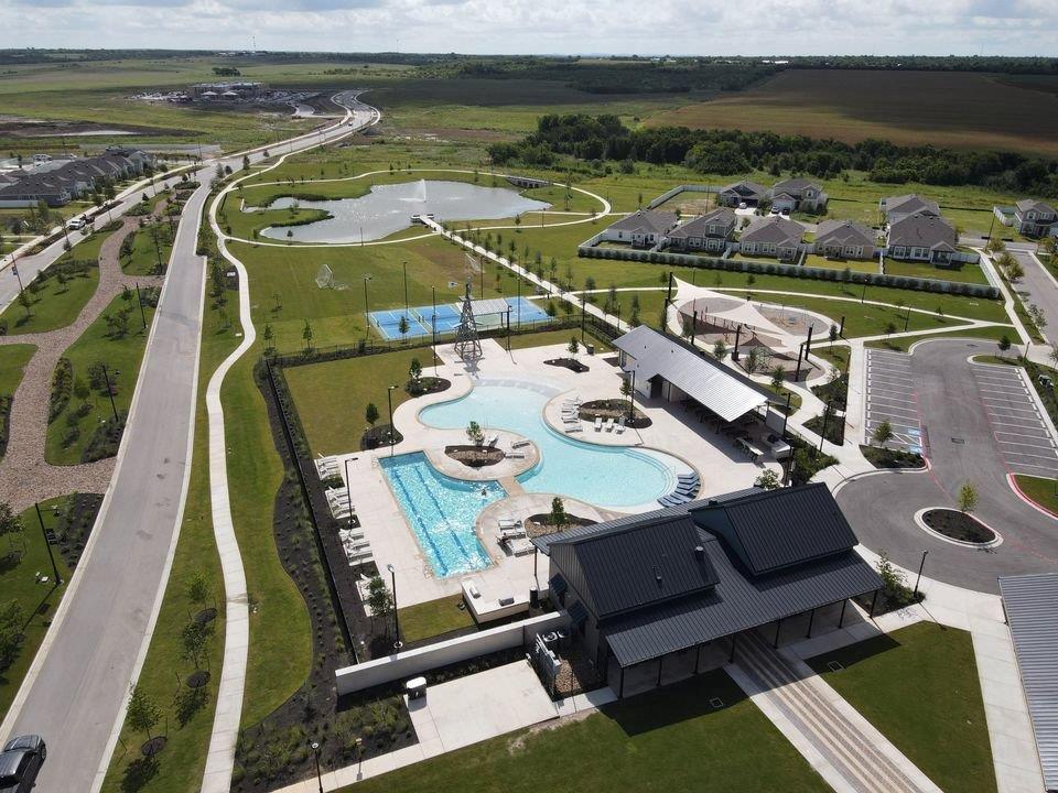 156 Huckleberry Lane Elgin, TX 78621 - Photo 10 of 16 An aerial view showcases a vibrant community with a winding road, expansive pool, and lush green spaces.