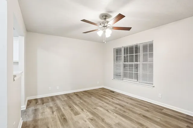 an empty room with wooden floor fan and windows