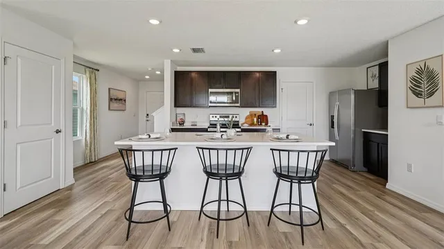 a kitchen with stainless steel appliances granite countertop a dining table chairs refrigerator and sink