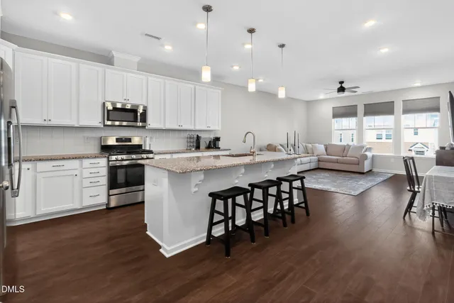 a kitchen with stainless steel appliances granite countertop a stove a sink a oven a dining table and chairs with wooden floor