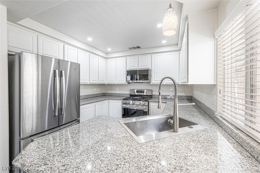 10133 Rice Paper Street Las Vegas, NV 89183 - Photo 14 of 36 Kitchen featuring NEW stainless steel appliances, recessed lighting, white cabinetry, hanging light fixtures, and light stone counters