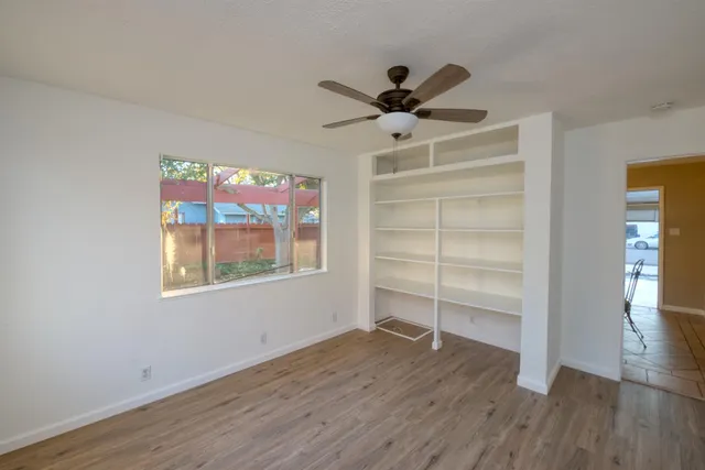 an empty room with wooden floor fan and windows