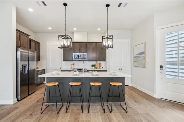 a kitchen with kitchen island a stove a refrigerator a sink a dining table and chairs with wooden floor