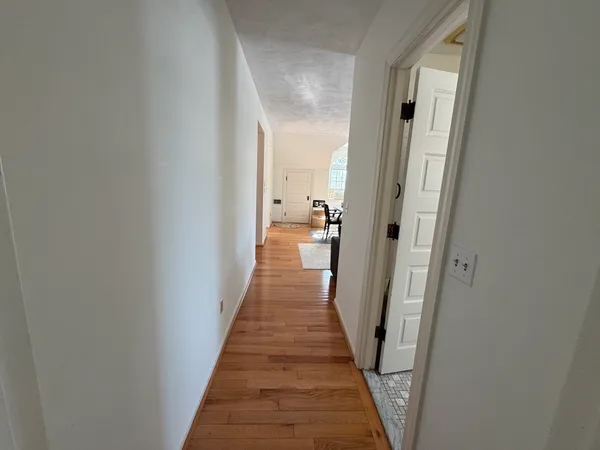 a view of a hallway with wooden floor and a bathroom