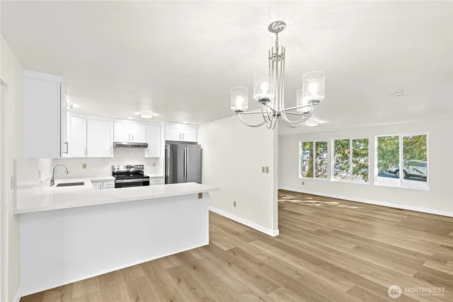 a view of a kitchen with stainless steel appliances granite countertop a stove a sink dishwasher a refrigerator white cabinets and wooden floor next to a window