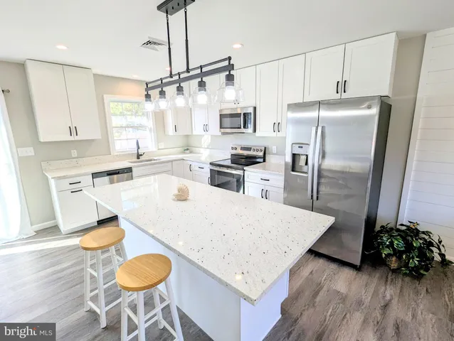 a kitchen with granite countertop a refrigerator a stove a sink dishwasher and white cabinets with wooden floor