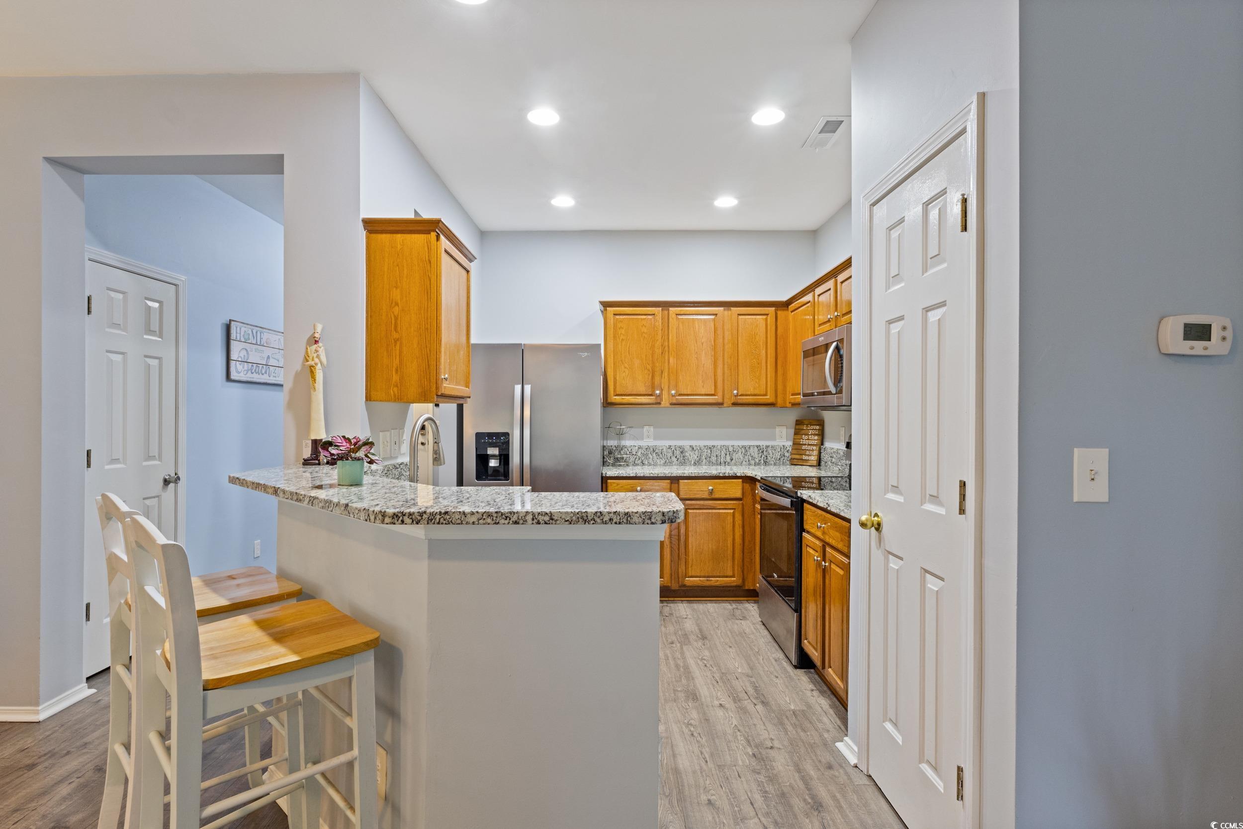 140 Olde Towne Way, Unit 2 Myrtle Beach, SC 29588 - Photo 14 of 40 Kitchen with brown cabinetry, a peninsula, light stone countertops, a breakfast bar, and appliances with stainless steel finishes
