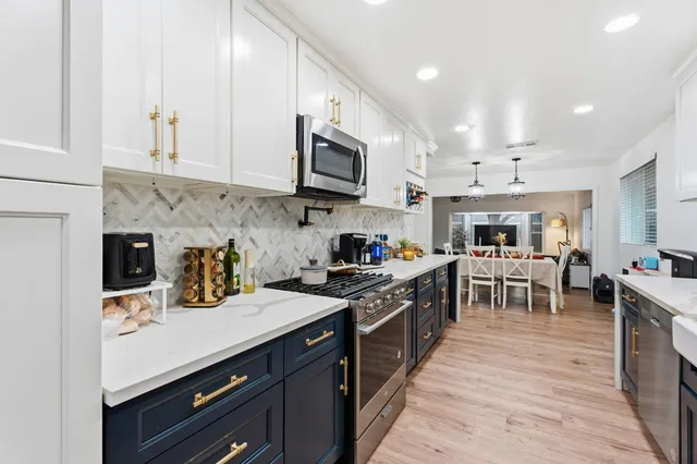 a kitchen with stainless steel appliances granite countertop a stove top oven a sink a dining table and chairs with white cabinets