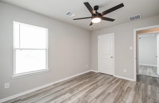 a view of empty room with wooden floor and fan