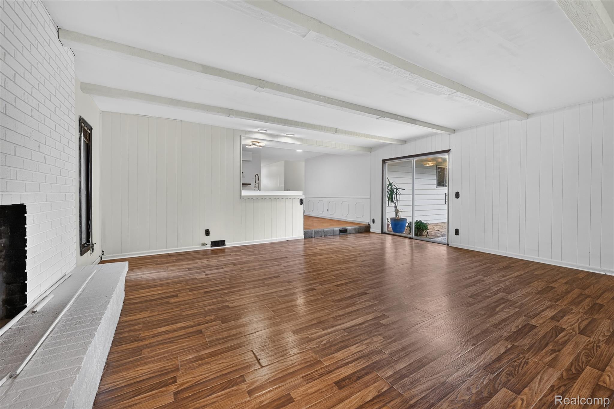 5457 Reid Road Swartz Creek, MI 48473 - Photo 21 of 51 Spacious room featuring wood-finish flooring, a white painted brick fireplace with hearth, and exposed white ceiling beams