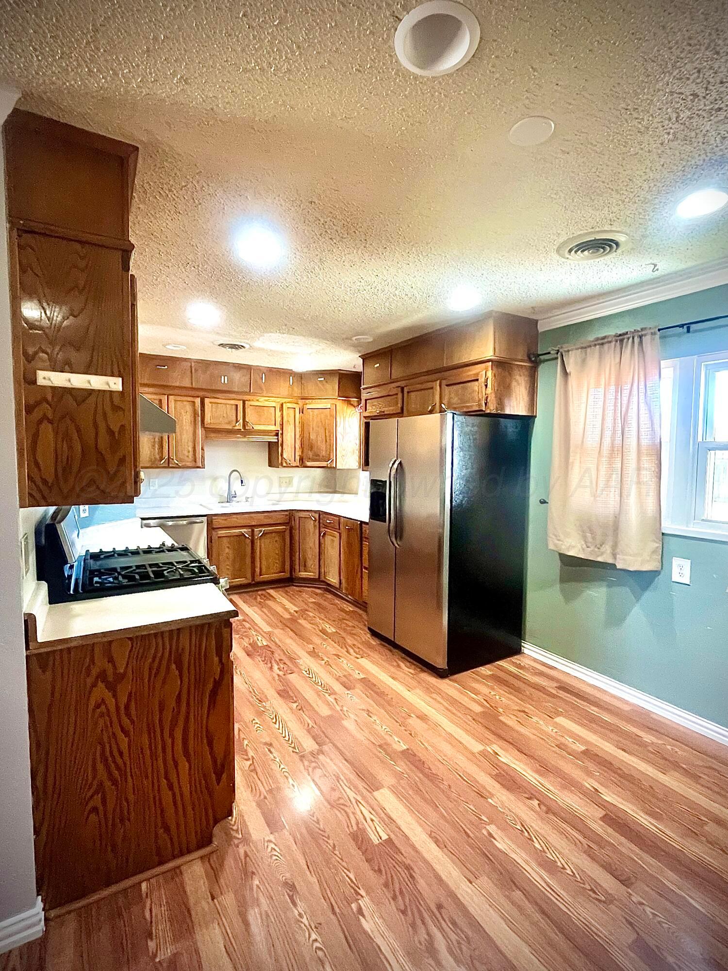 5116 Crockett Street Amarillo, TX 79110 - Photo 6 of 23 a kitchen with stainless steel appliances granite countertop a refrigerator a stove and a sink with wooden floor