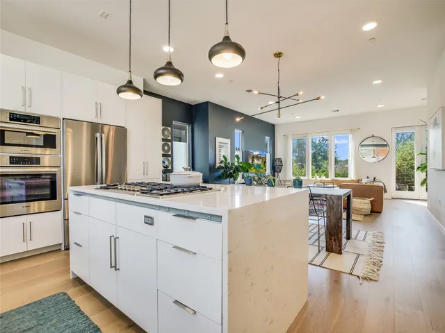 a kitchen with stainless steel appliances granite countertop a stove a refrigerator a oven a dining table and chairs with wooden floor