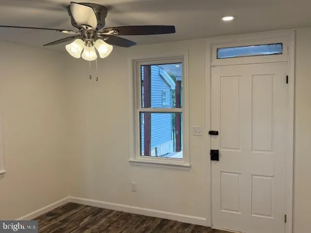 a big room with wooden floor a ceiling fan and kitchen view