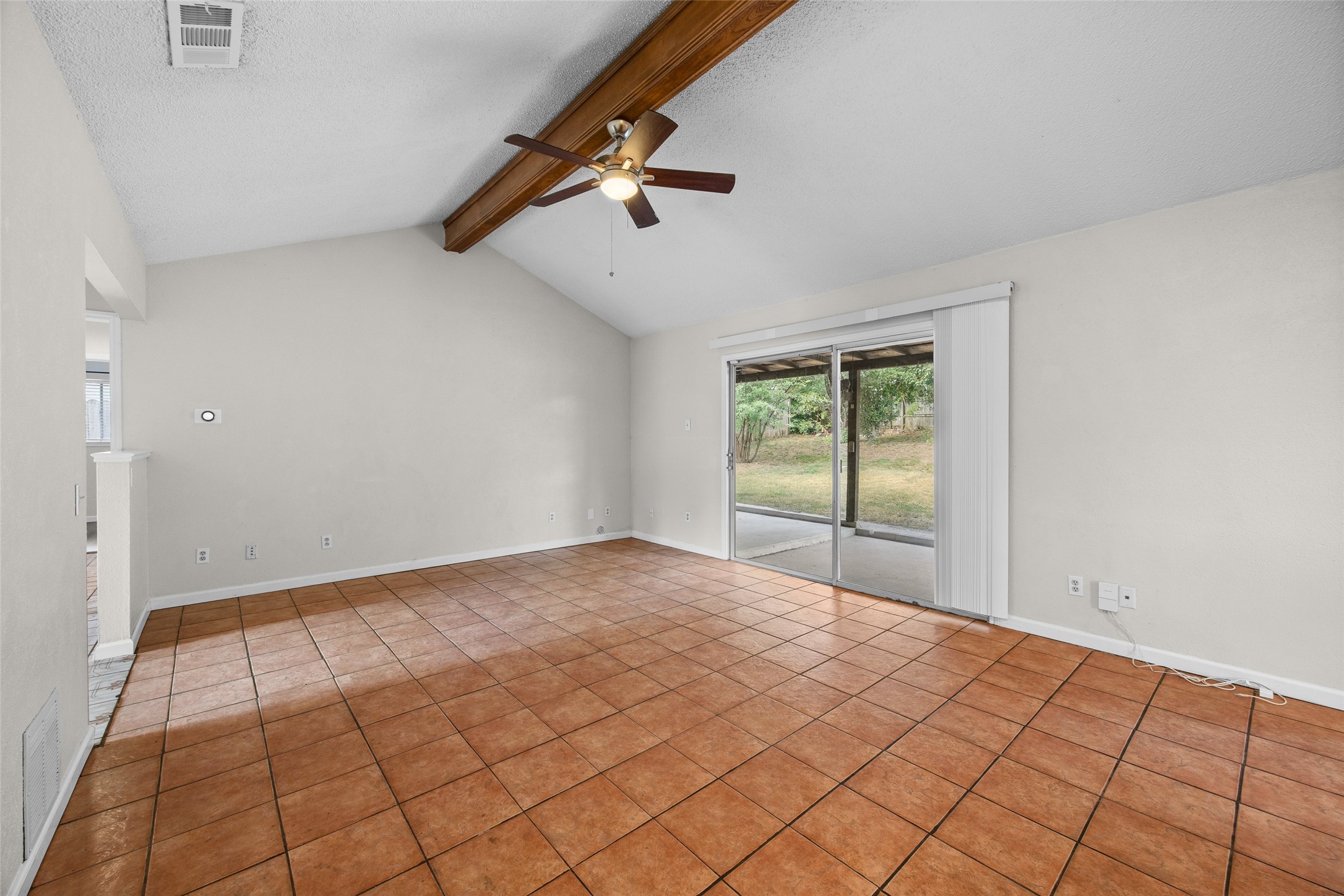7506 Glenhill Road Austin, TX 78752 - Photo 7 of 20 A spacious living area features vaulted ceilings, tile flooring, and sliding glass doors leading to a serene outdoor space.